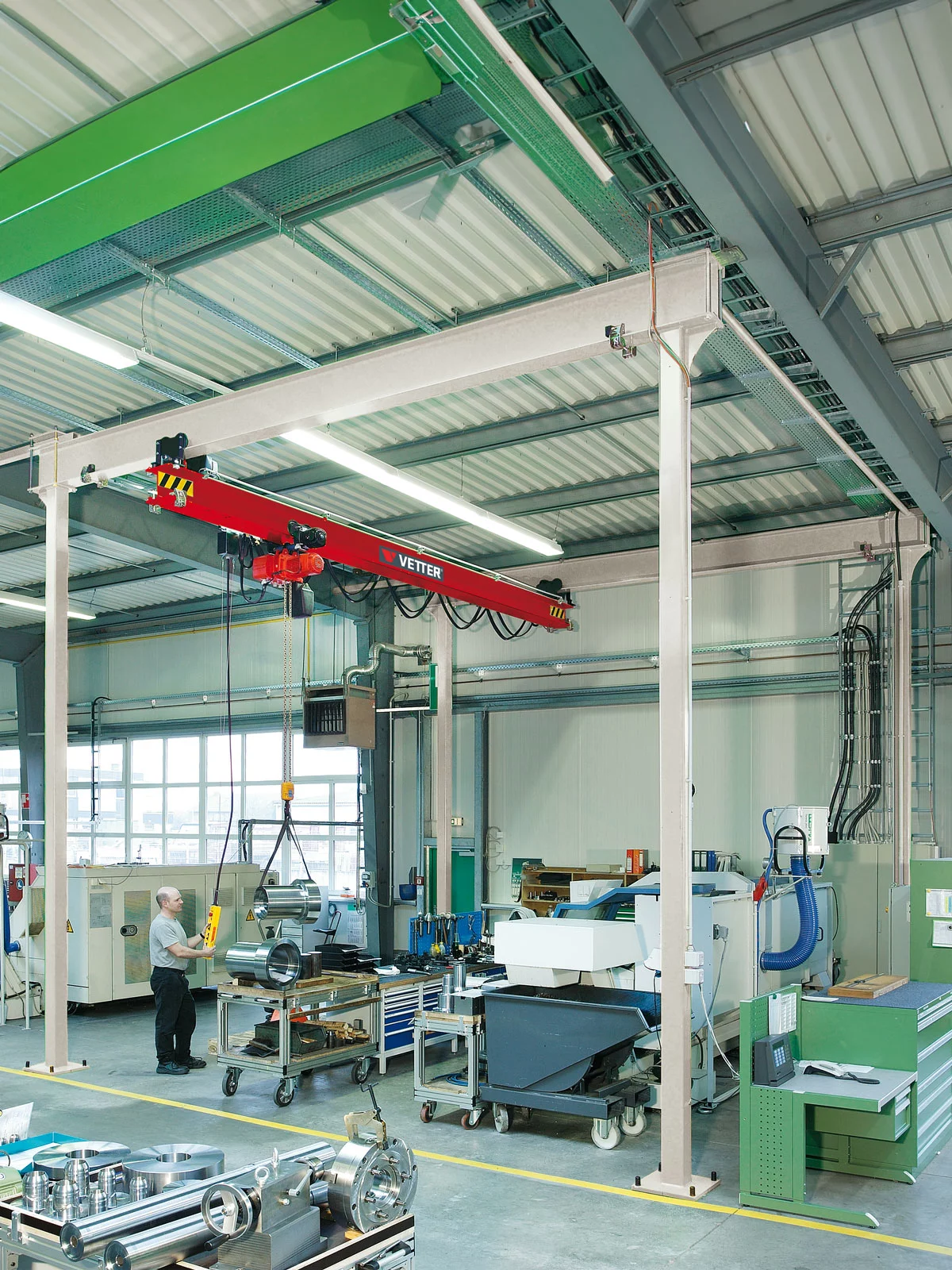 ZSP-E Portalkran im Bearbeitungszentrum. In einer Nahaufnahme bewegt ein Mitarbeiter mithilfe des Krans Metallteile an einem Arbeitsplatz.