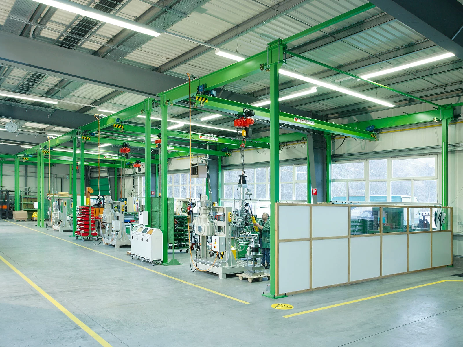 Einblick in eine Maschinenbauhalle mit mehreren grüne ZSP-E Portalkransystemen – jeder Arbeitsplatz ist mit einem eigenen Kransystem ausgestattet.