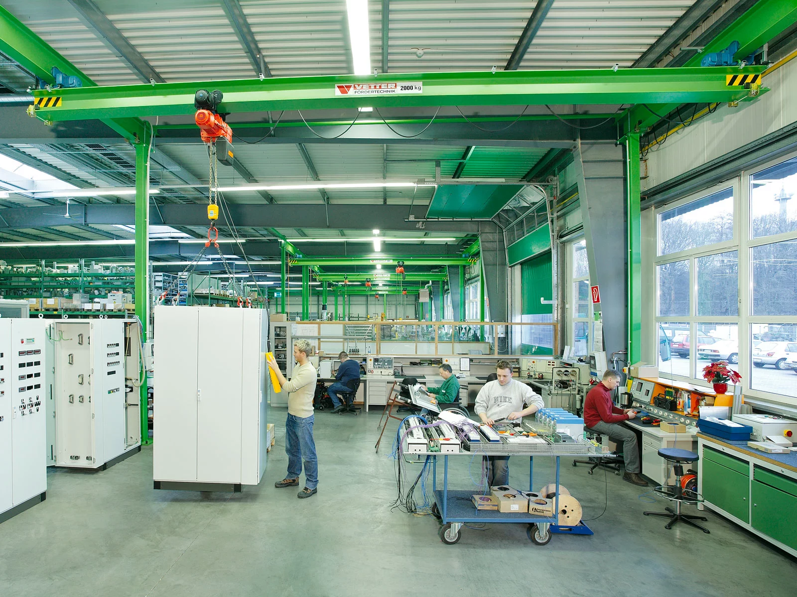 Einblick in eine Maschinenbauhalle mit mehreren grünen ZSP-E Portalkransystemen – jeder Arbeitsplatz ist mit einem eigenen Kransystem ausgestattet.