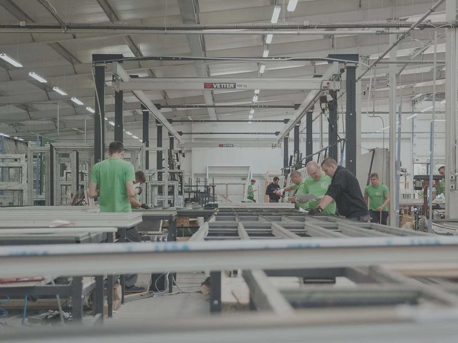 Zwei ZSP-ErgoLine Leichtkransysteme in einer Fensterfertigung. Mehrere Mitarbeiter arbeiten an der Produktionslinie.