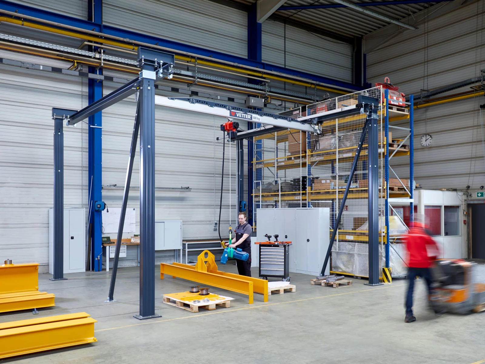 ZSP-ErgoLine Leichtkransystem in einer Fertigungshalle. Ein Mitarbeiter in Arbeitskleidung hebt ein Metallteil.