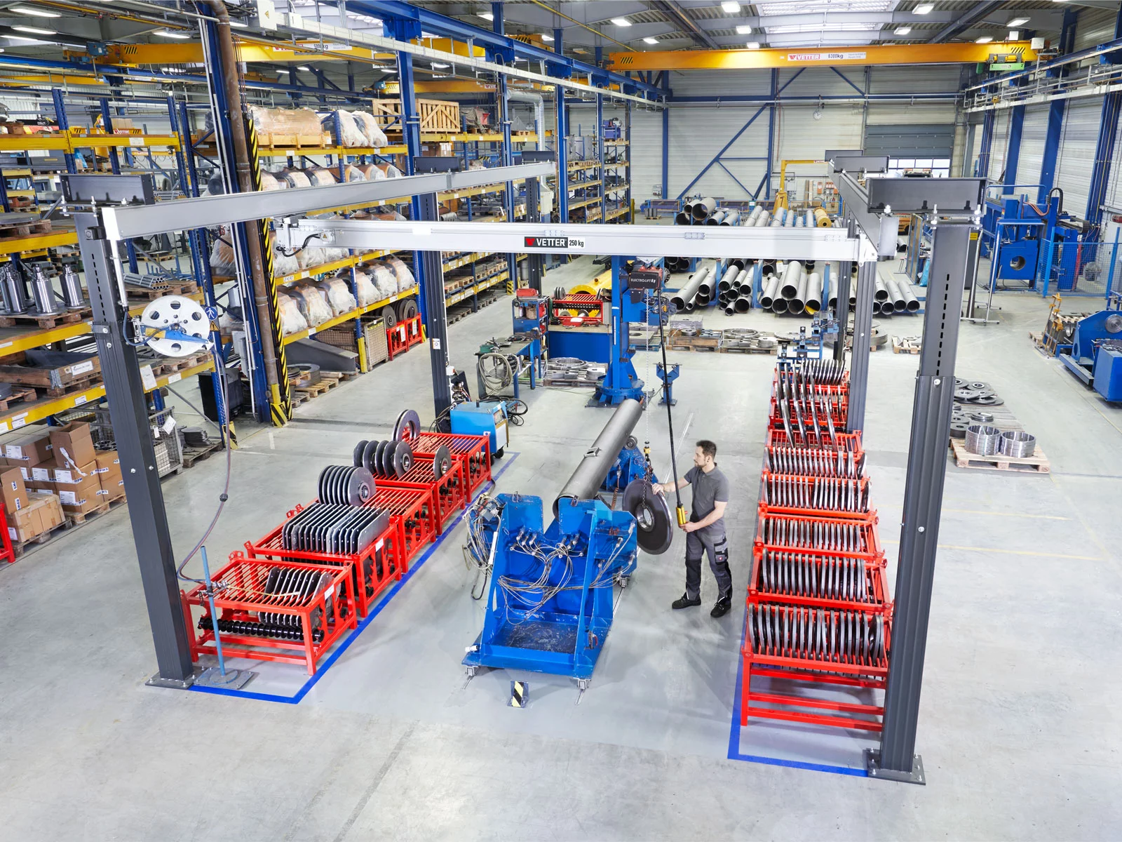 ZSP-ErgoLine Leichtkransystem in einer Fertigungshalle. Ein Mitarbeiter in Arbeitskleidung hebt ein Metallteil.