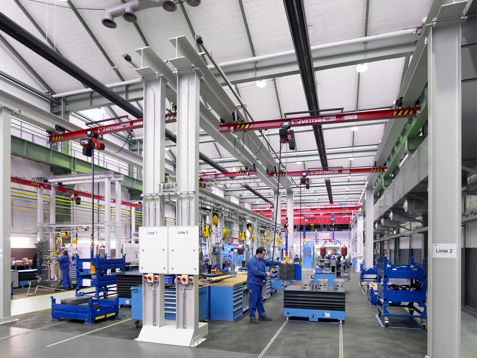 ZSP-M Portalkran mit lichtgrauen Stützen und roter Brücke im Anlagenbau. Ein Mitarbeiter bedient das Hebezeug über eine Kommandotafel.