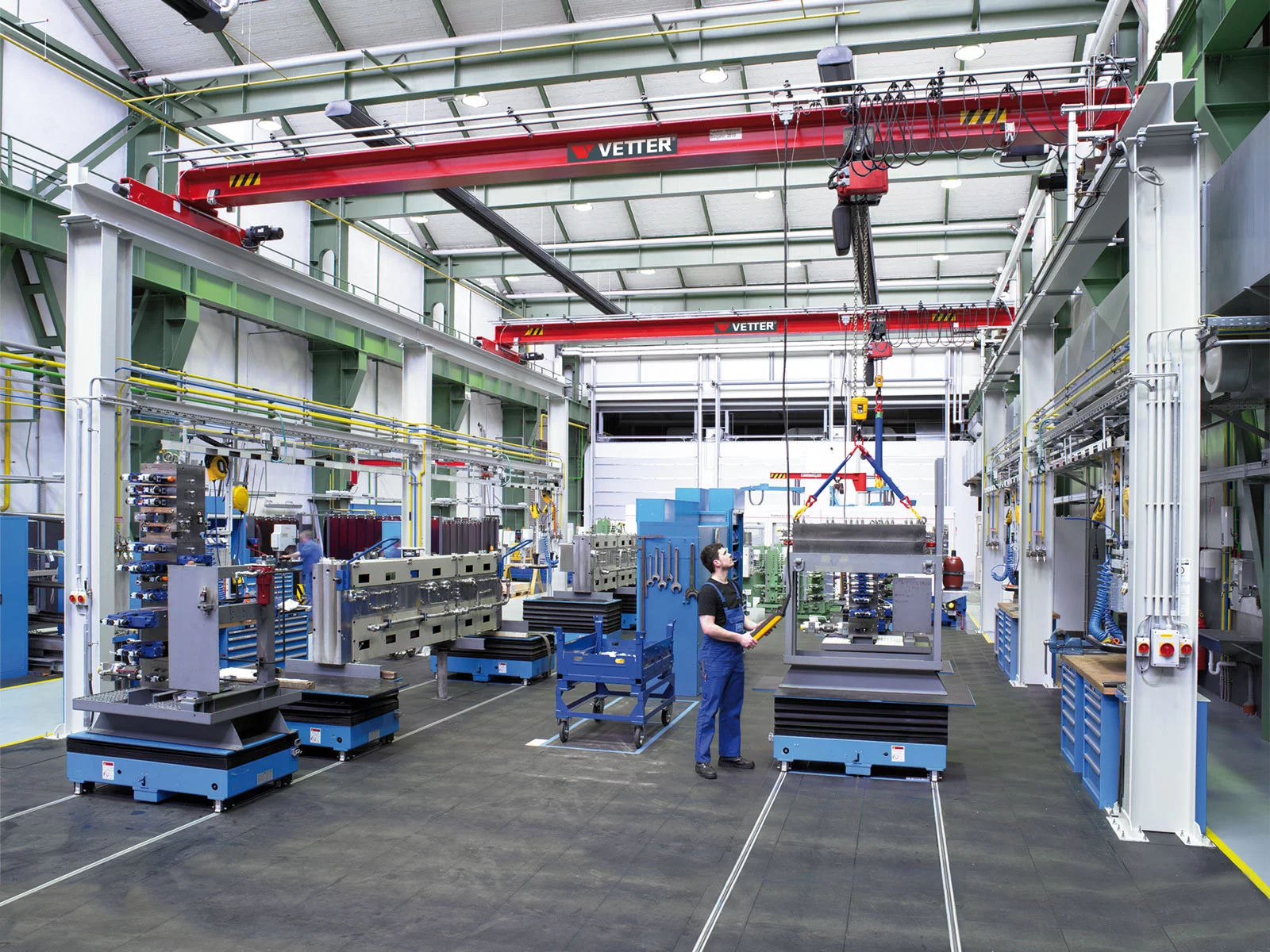 ZSP-Olympia Portalkran mit lichtgrauen Stützen und roter Brücke in einer modernen Fertigungshalle. Ein Mitarbeiter bedient eine Kommandotafel zur Maschinenbeschickung.