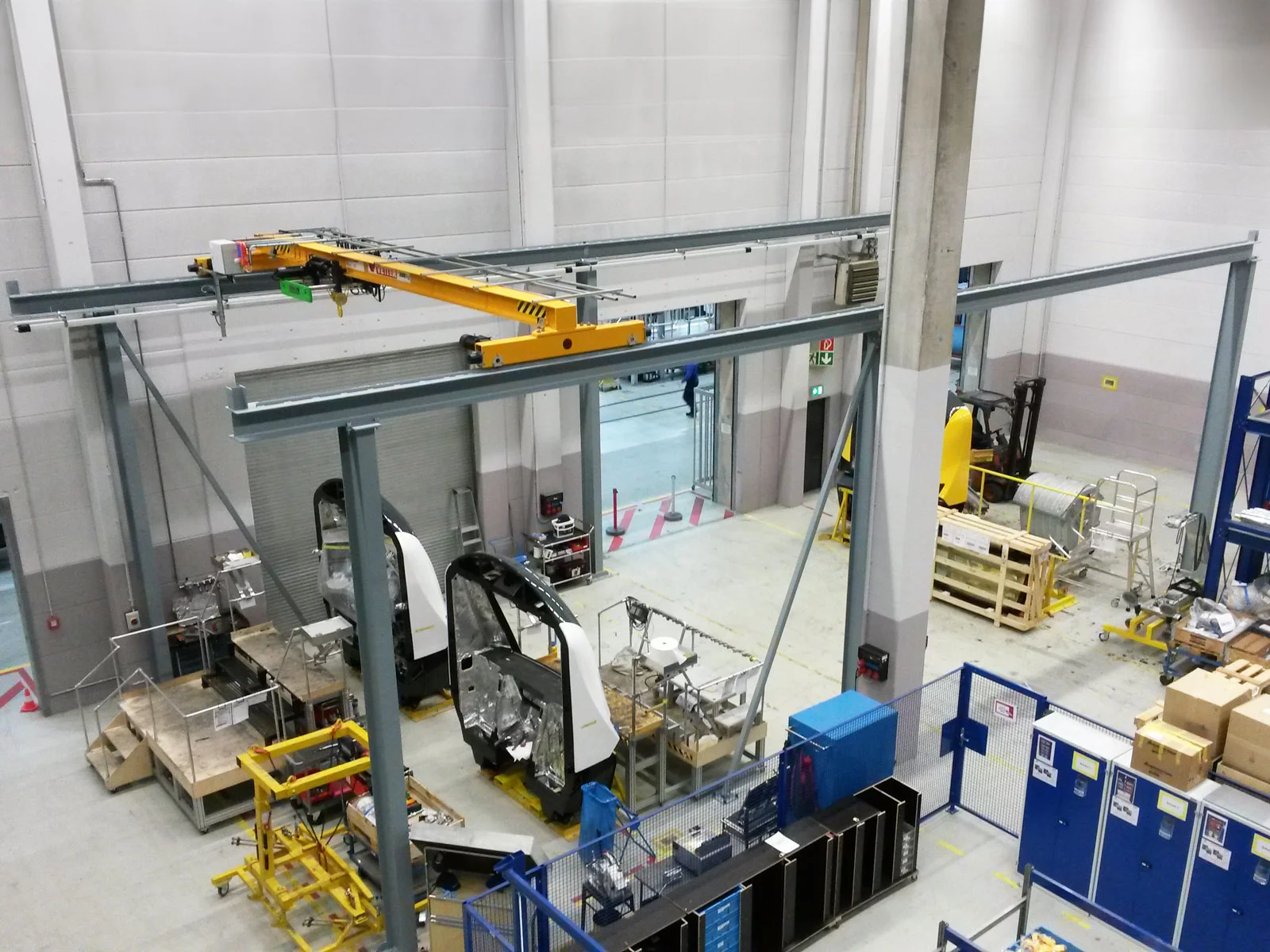 ZSP-Olympia Portalkran in Stahlfarbe mit gelber Brücke in einer automatisierten Fertigung. Die Fahrbahn ist auf der einen Seite länger als auf der anderen.