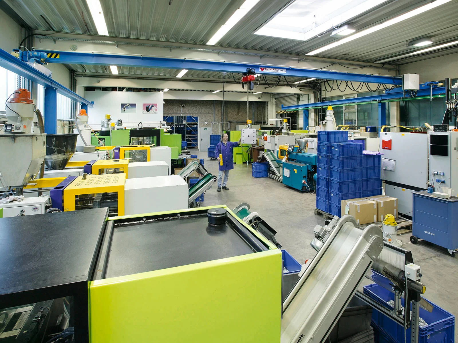 Blauer ZSP-Olympia Portalkran in einer Halle der verarbeitenden Industrie. Ein Mitarbeiter in Arbeitskleidung bewegt ein Bauteil mit dem Kran.