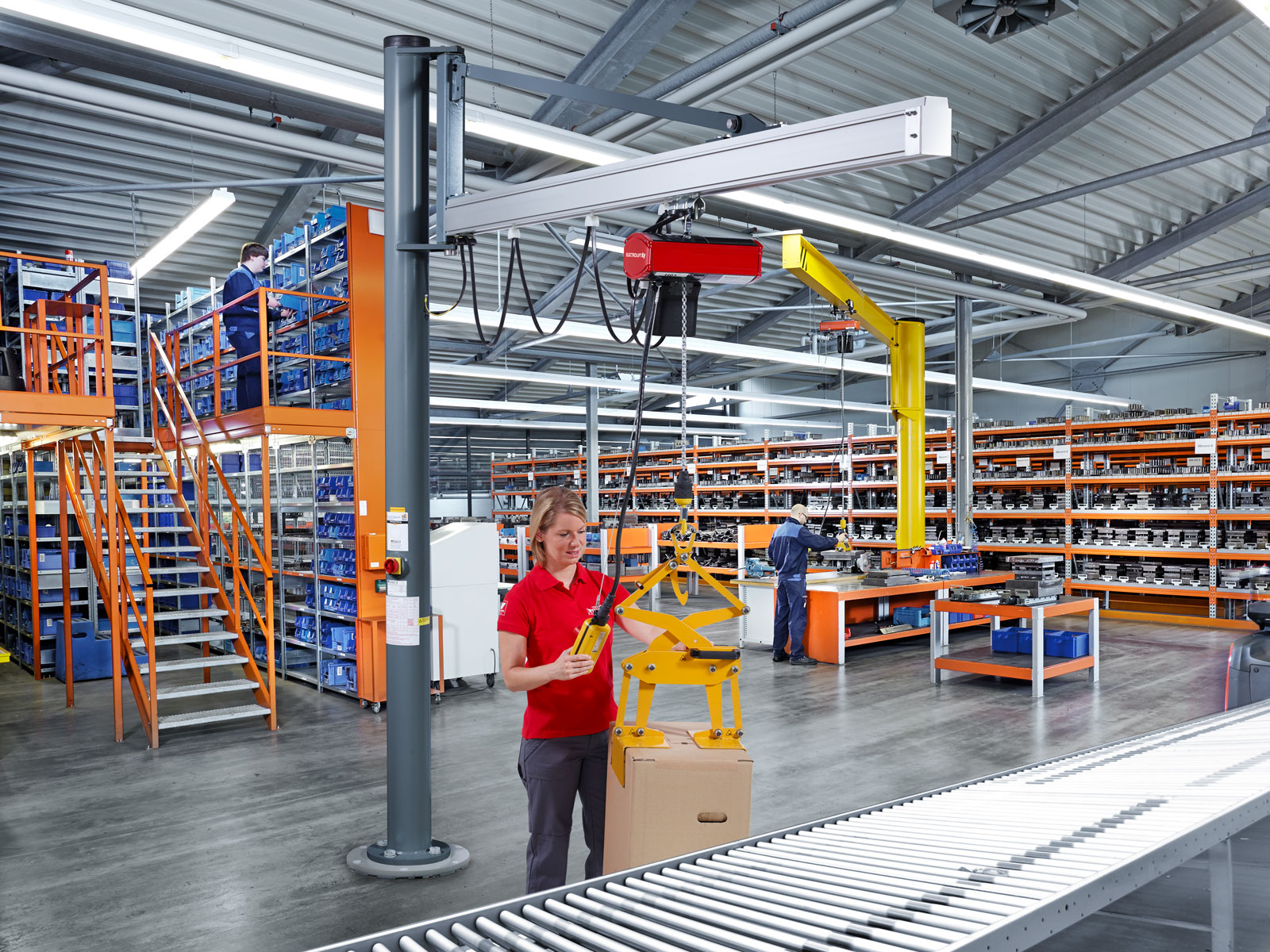 Eine junge Frau bedient mithilfe einer Kommandotafel einen Säulenschwenkkran vom Typ US an einer Packstation in einem Lager