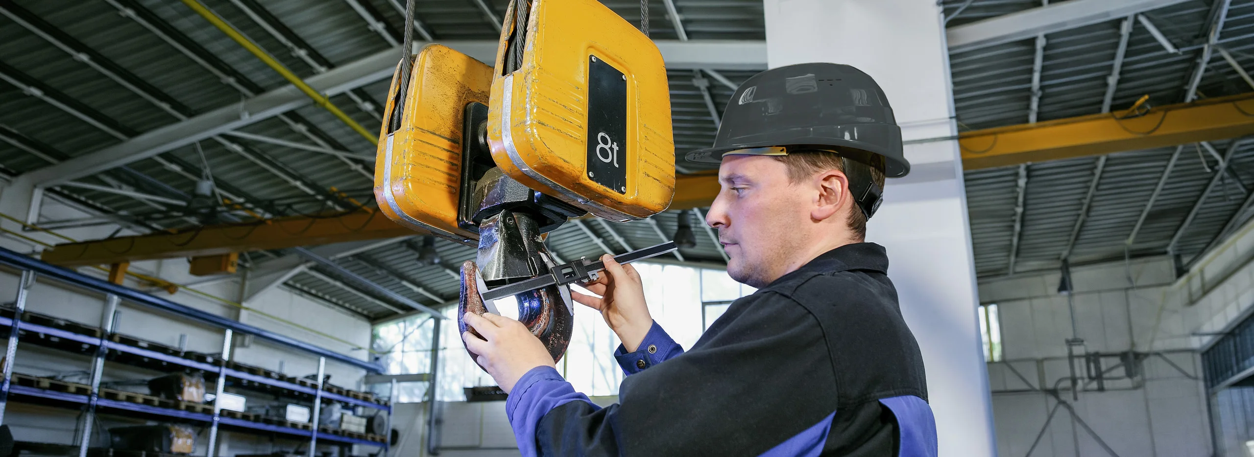 Mitarbeiter in Arbeitskleidung f&uuml;hrt Service und Montagearbeiten an einem Kranhaken durch