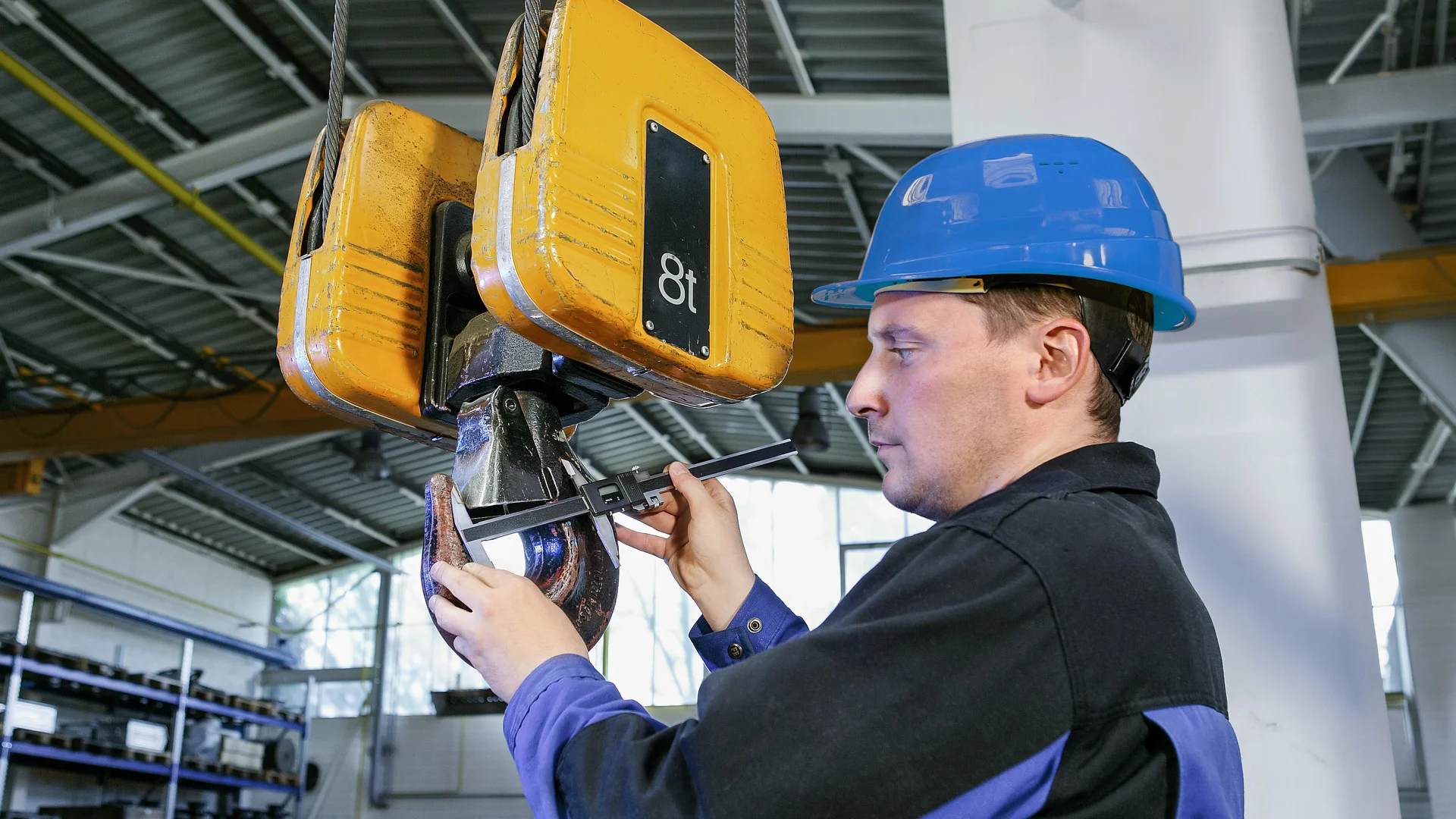 Mitarbeiter in Arbeitskleidung f&uuml;hrt Service und Montagearbeiten an gelbem Hallenkran durch